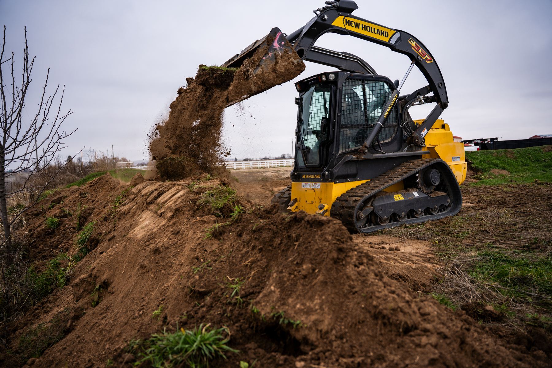Skid steer dumping a full bucket of topsoil.