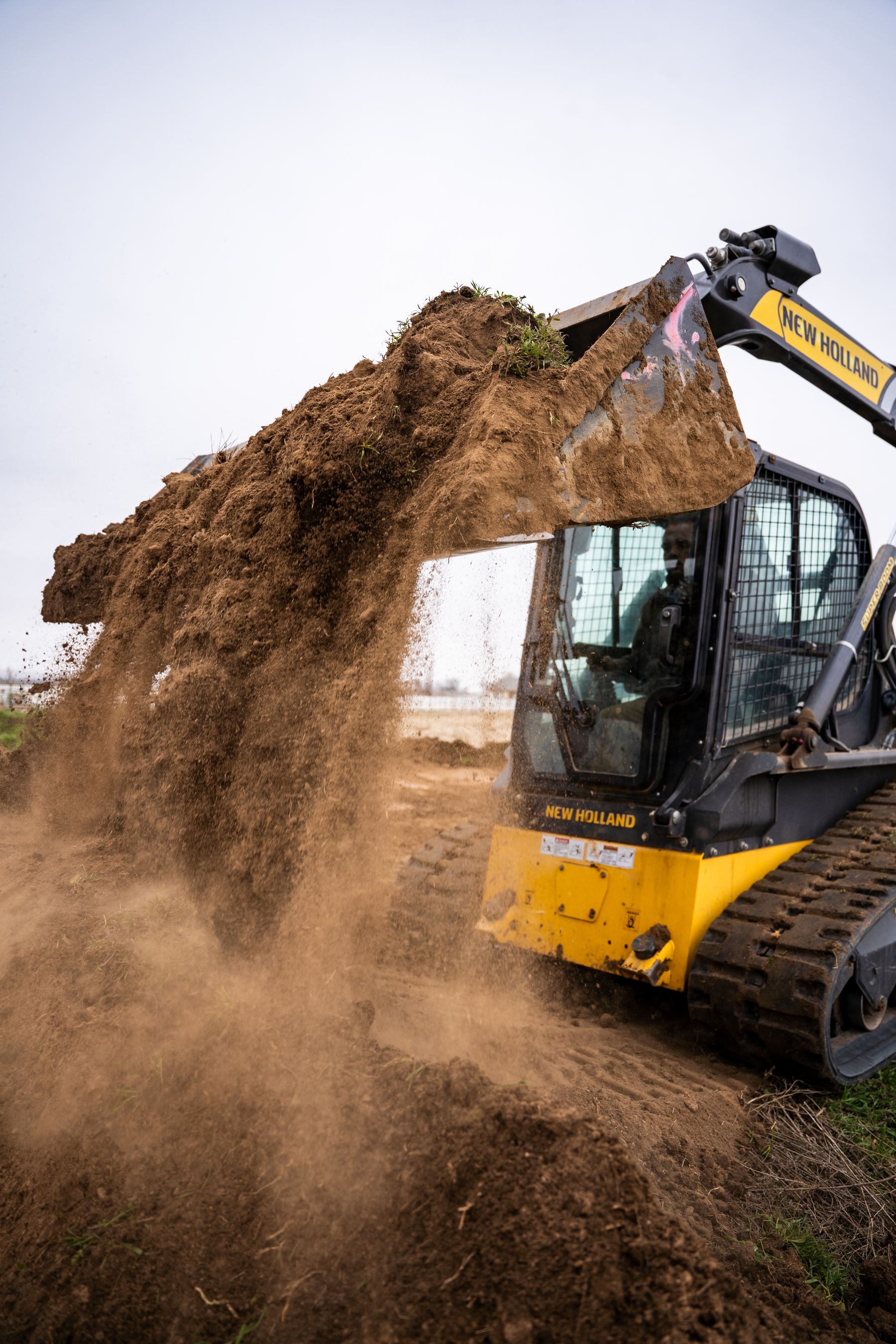 Compact track loader dumping sod and dirt on site.
