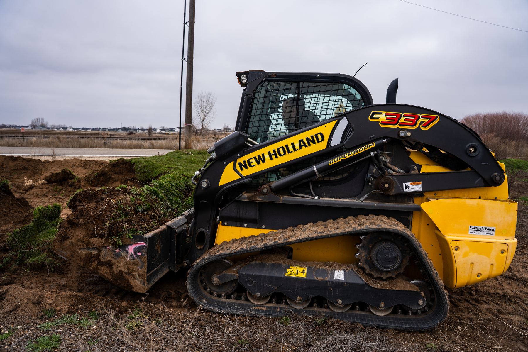 Compact track loader digging along a roadside ditch.