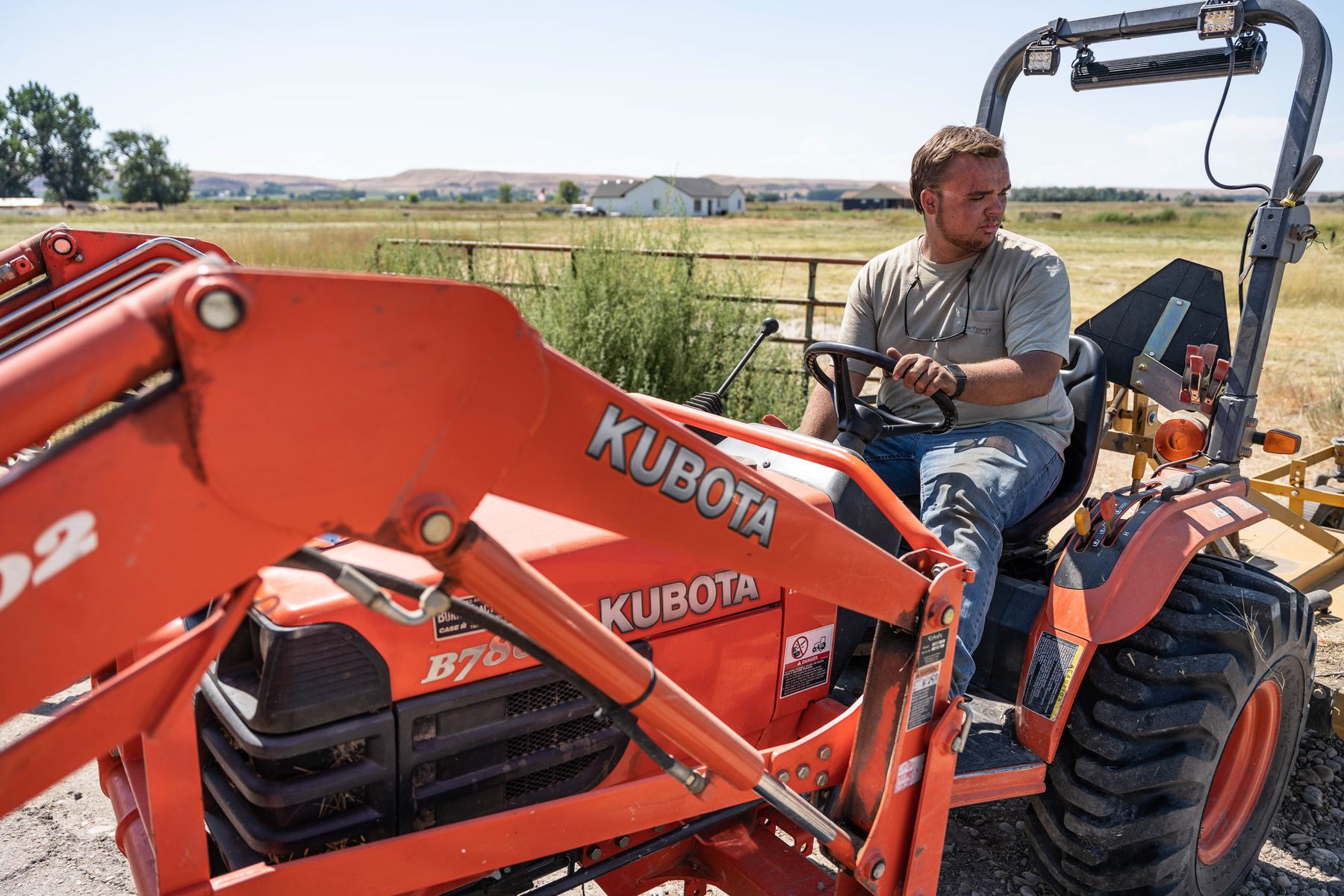 A Kubota tractor with front loader working a rural property.