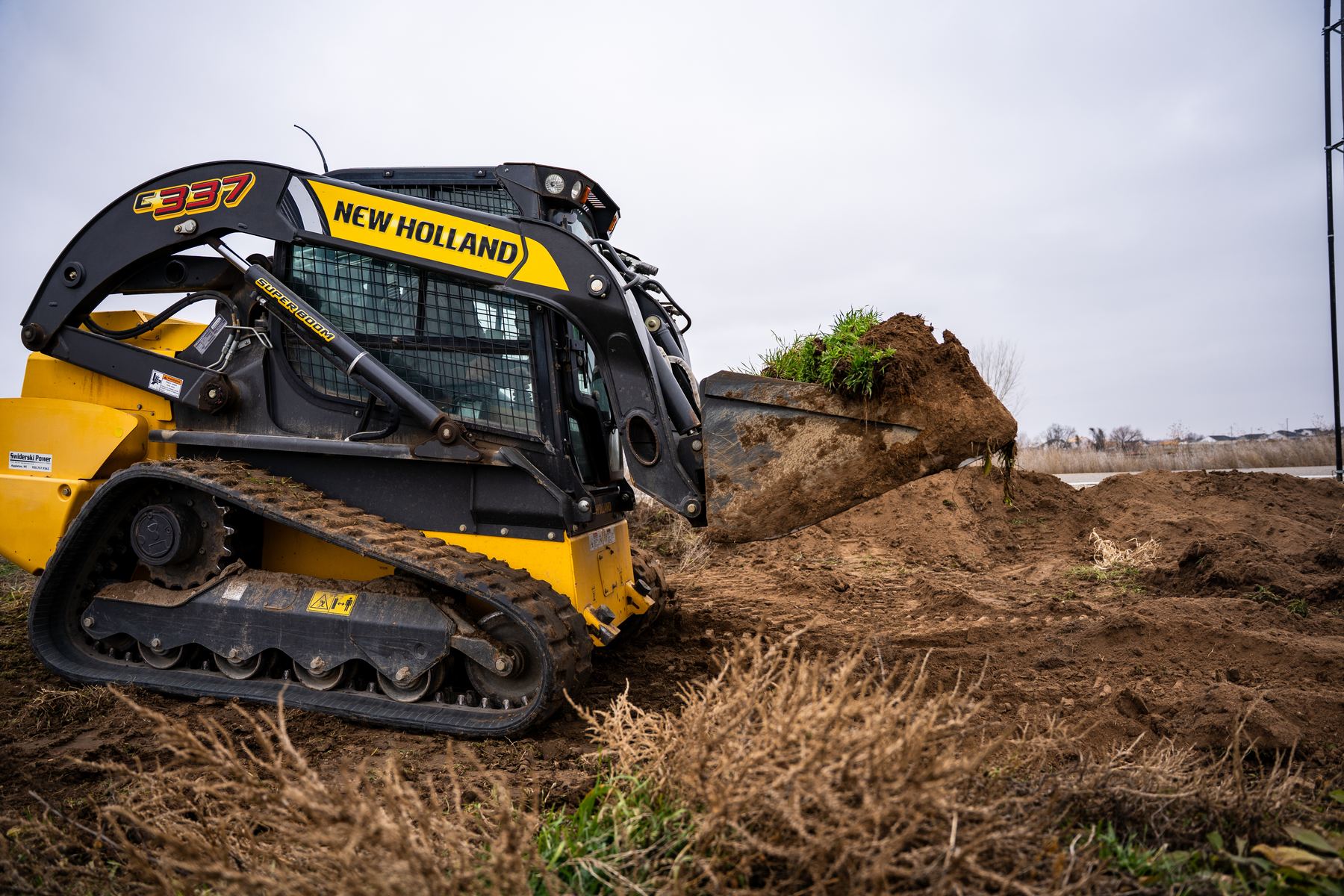 Compact track loader lifting a bucket of sod and dirt.
