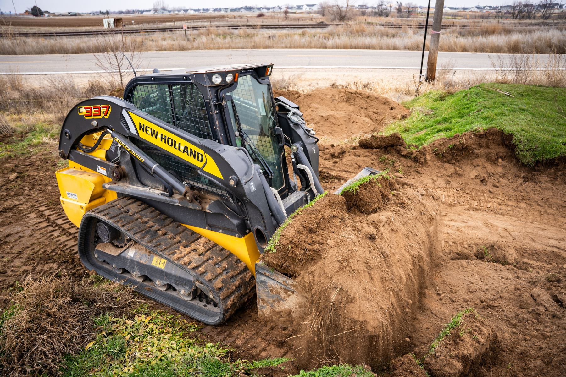 Compact track loader grading a berm along a roadside.