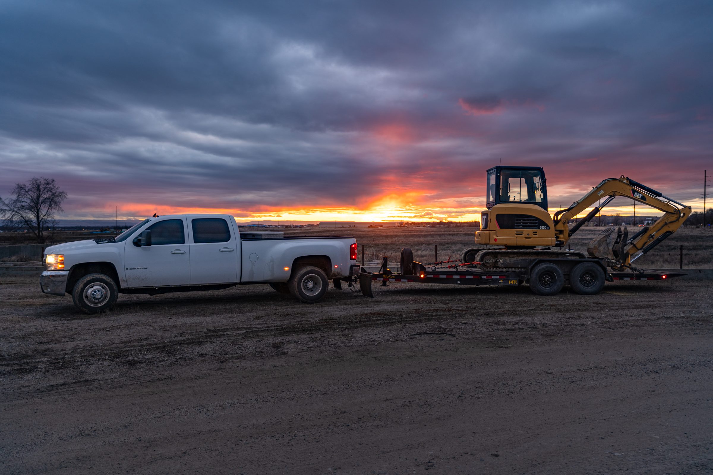 Truck and trailer hauling equipment at sunset.